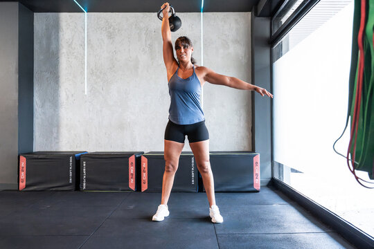 Female athlete performing kettlebell overhead press in gym