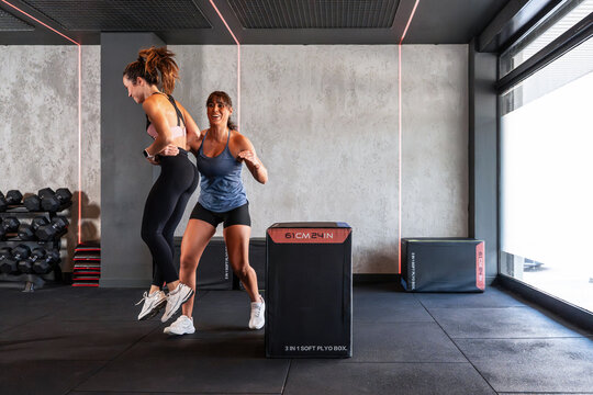 Women doing plyometric box jump with coach in modern gym