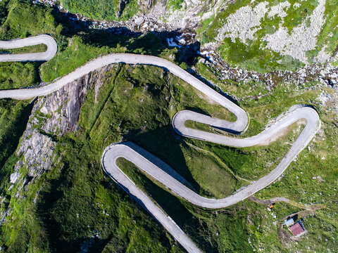 Aerial view of the historic Tremola winding road with its iconic hairpin turns snaking through the green alpine slopes and rocky terrain of the Gotthard Pass in Airolo, Ticino, Switzerland.