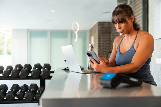 Woman using smartphone and laptop in modern gym interior