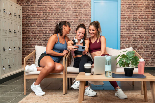 Friends resting after workout, checking phone in gym lounge