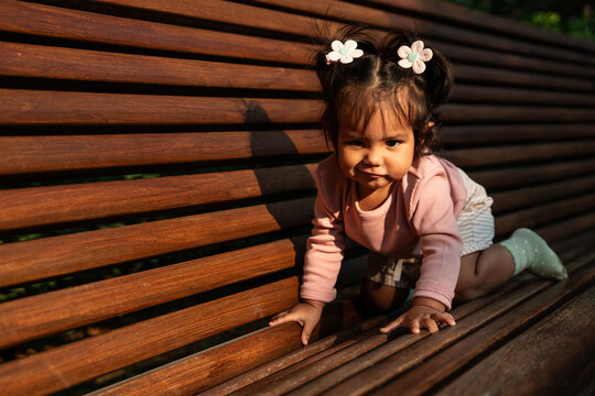 Latin baby girl crawling on wooden bench in sunlight