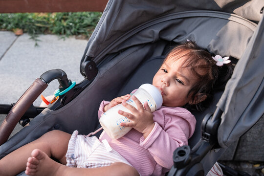 Latin baby girl drinking milk bottle in stroller outdoors