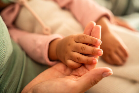 Latin mother holding baby daughter hand in warm closeup