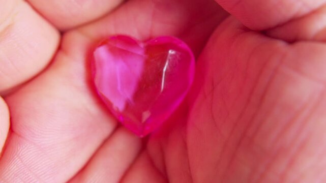 Cinematic macro shot of a pink glass heart in a hand.Soft daylight. Simbol of fragility, emotional support, self-love, empathy, care and vulnerability.