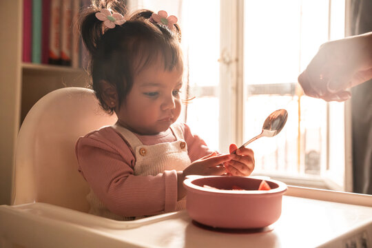 Latin mother feeding baby daughter in sunny kitchen scene