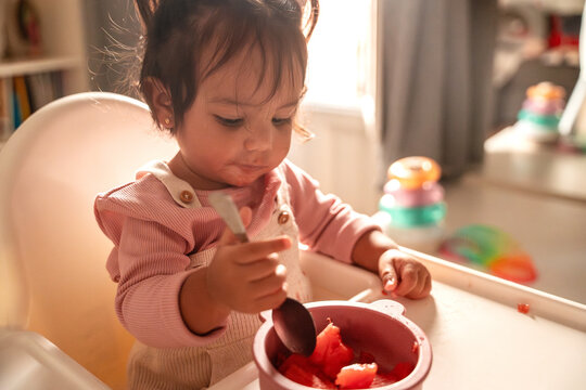 Latin baby girl eating fruit in high chair at home
