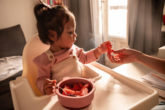Latin mother feeding baby daughter watermelon at home