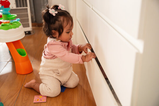 Latin baby girl exploring drawer in home interior setting