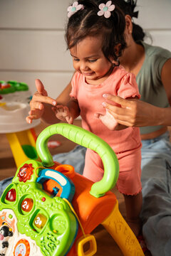 Latin mother helping baby daughter take first steps indoors