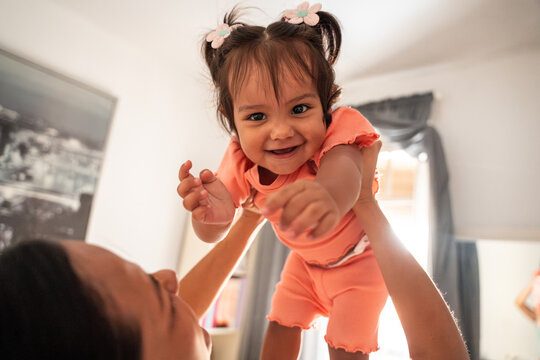 Latin mother lifting baby daughter at home in daylight