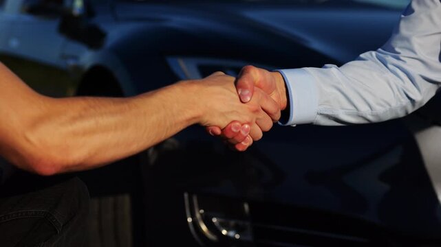 Male hand giving key of car to buyer of electric automobile outdoor. Handshake between salesman and new owner of modern auto after successful deal. Concept of buy or rent car. Slow mo
