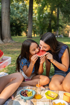 Two sisters enjoying watermelon at a sunny park picnic