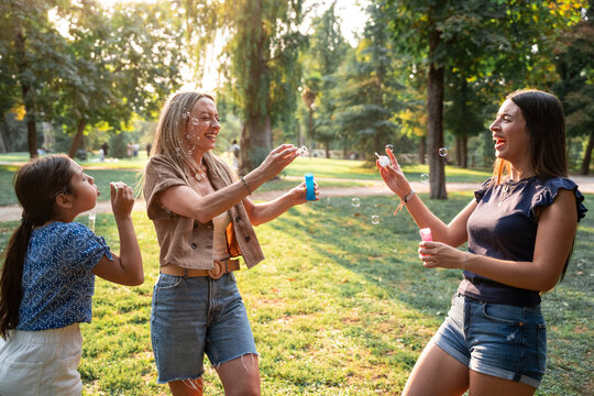 Mother and daughters blowing bubbles together in a park