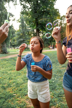 Sisters blowing bubble in park on sunny summer day outdoors