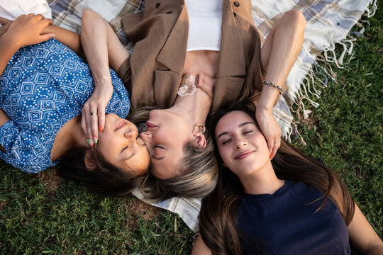 Mother relaxing with daughters on blanket during park picnic