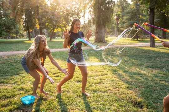 Mother and daughters playing with giant soap bubble in park