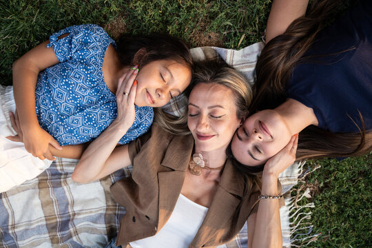 Mother resting with daughters on picnic blanket outdoors