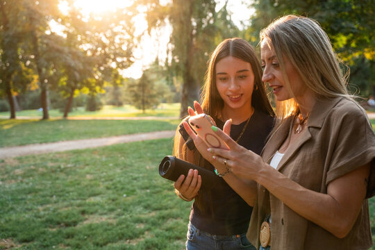 Mother and daughter using smartphone with speaker in park