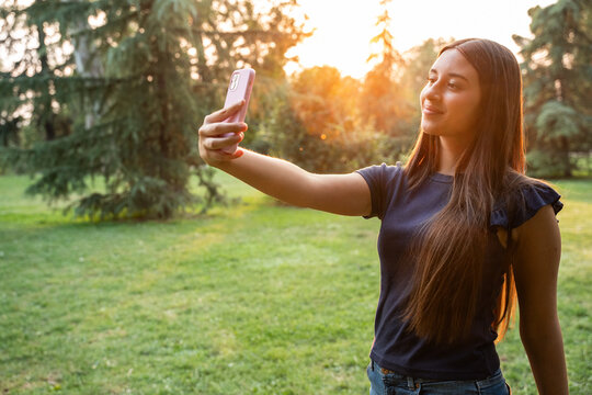 Teenager taking smartphone selfie in park at sunset light