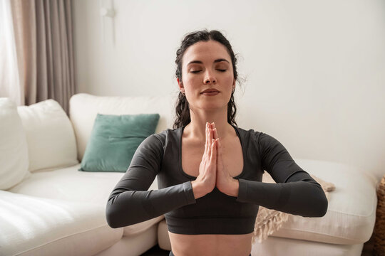 Woman meditating with prayer hands on sofa at home