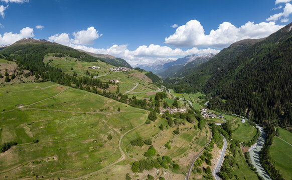 Aerial view of the lush green Engadin valley with winding roads, a flowing river, and alpine villages under a blue sky in Zernez, Grisons, Switzerland.
