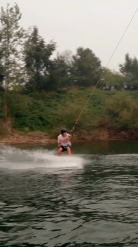Vertical video: Cable pulling wakeboarder wearing helmet, shorts, grinding obstacle on lake for fun