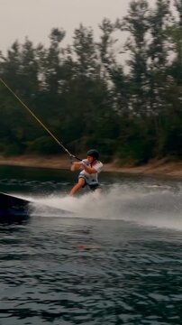 Vertical video: Cable pulling rider carving lake jumping kicker doing air grab to land trick helmet