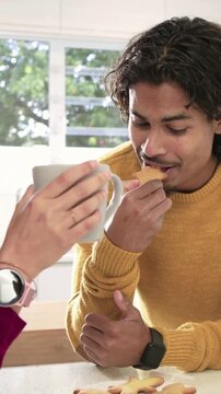 Vertical video: Leaning man chatting with woman in knits at home with grey mug, eating star cookie