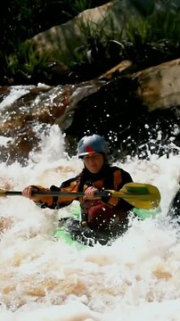 Vertical video: Entering foamy drop helmeted kayaker paddling to steer green kayak in river