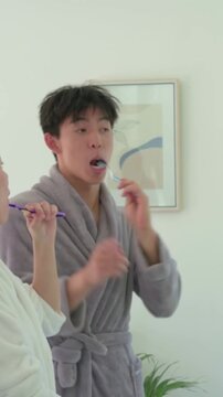 Vertical video: Picking up brushes couple brushing teeth at bathroom sink in robes headband morning