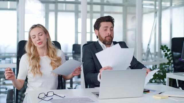 Carefree two Caucasian business man with woman singing working with corporate documentation at office table joyful businessman with businesswoman dancing sing reviewing documents dance entertainment