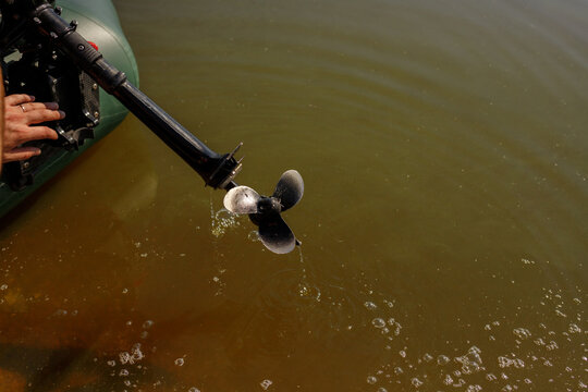 Black outboard engine motor installed on transom of green inflatable PVC boat in calm lake water, propeller detail close up, fisherman equipment preparation, active outdoor water recreation, copy spac