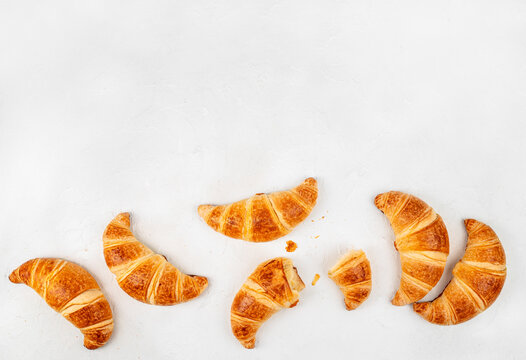Bitten Croissant Among Fresh Croissants on White Background Top View