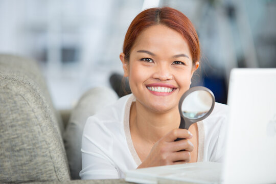 young woman looking at her laptop with a magnifying glass