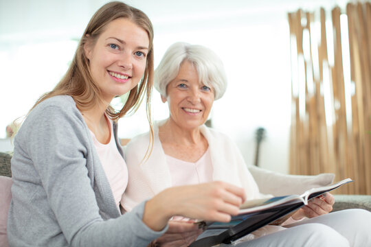 smiling daughter visit the senior mother looking at photo album