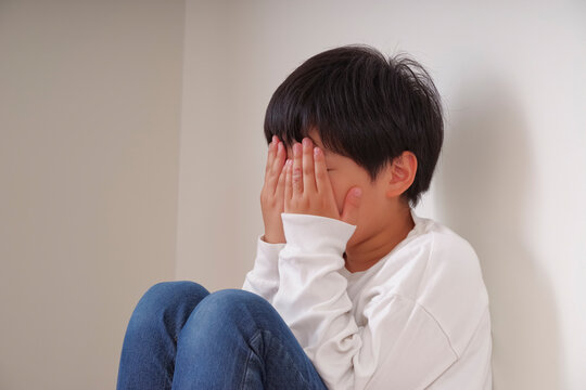 壁際で膝を抱えてうずくまる男の子