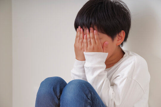 壁際で膝を抱えてうずくまる男の子