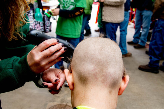 Woman uses electric clippers to shave the head of a participant during a community head-shaving event, illustrating charity, solidarity, fundraising, and support with faces not visible.