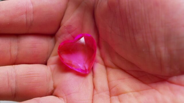 Cinematic macro shot of a pink glass heart in a hand.Soft daylight. Simbol of fragility, emotional support, self-love, empathy, care and vulnerability.