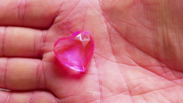 A small pink glass heart in a open palm.Close-up, natural light, cinematic.Perfect  simbol for romantic love, Valentine's Day, trust and tenderness.