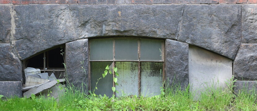An arched basement window with broken glass