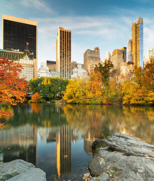 Autumn foliage and skyscrapers reflect in The Pond, highlighting a premier tourism destination and urban travel escape in Central Park, Manhattan, New York City.