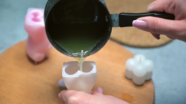 Person pouring melted wax into a decorative silicone candle mold.