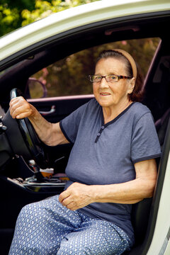 Old woman driving a car in the countryside, road trip concept.  Portrait of an old woman driving and near a car, on a walk outside the city.