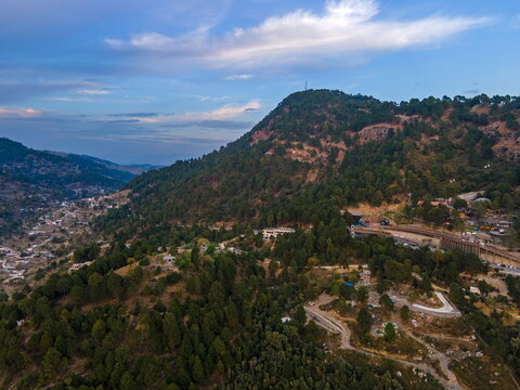 Aerial view of Dino Valley theme park nestled in the lush green Margalla Hills with winding roads and scattered buildings under a soft blue sky in Islamabad, Islamabad Capital Ter, Pakistan.