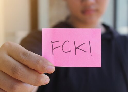 Hand holding a pink sticky note with FCK! text, representing youth frustration, social outrage, and systemic failure for activism or protest concepts