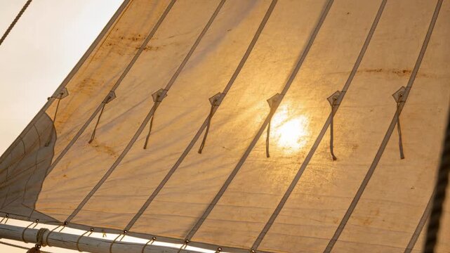 Billowing tan canvas sail responding to light gust onboard boat, showing rope tails, battens