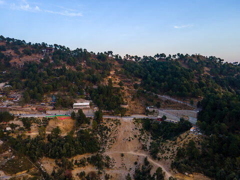 Aerial view of Dino Valley theme park nestled on a lush green hillside with winding roads and dense forest under a clear sky Islamabad, Islamabad Capital Territory, Pakistan.