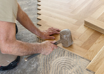 Worker installing herringbone parquet flooring with rubber mallet during hardwood floor installation